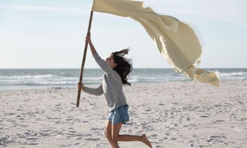 Girl walking across beach with a fabric flag