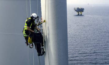 Man i skyddsutrustning klättrar på rotorblad i ett havsbaserat vindkraftverk
